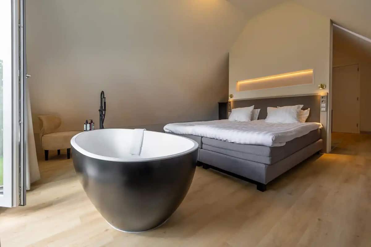A modern bedroom with a large round table, a bed with a headboard, and a door leading to another room.