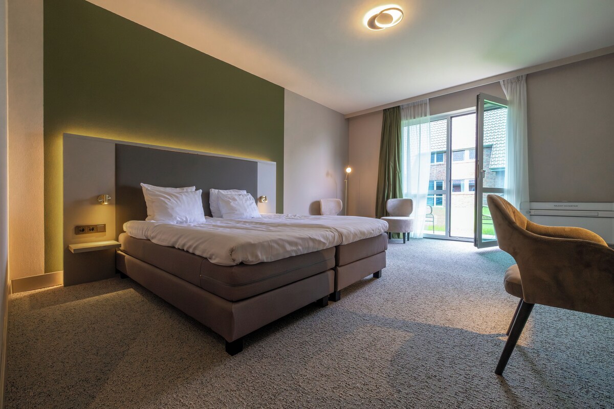 A hotel room with a bed, a chair, a desk, and a view of the outside.