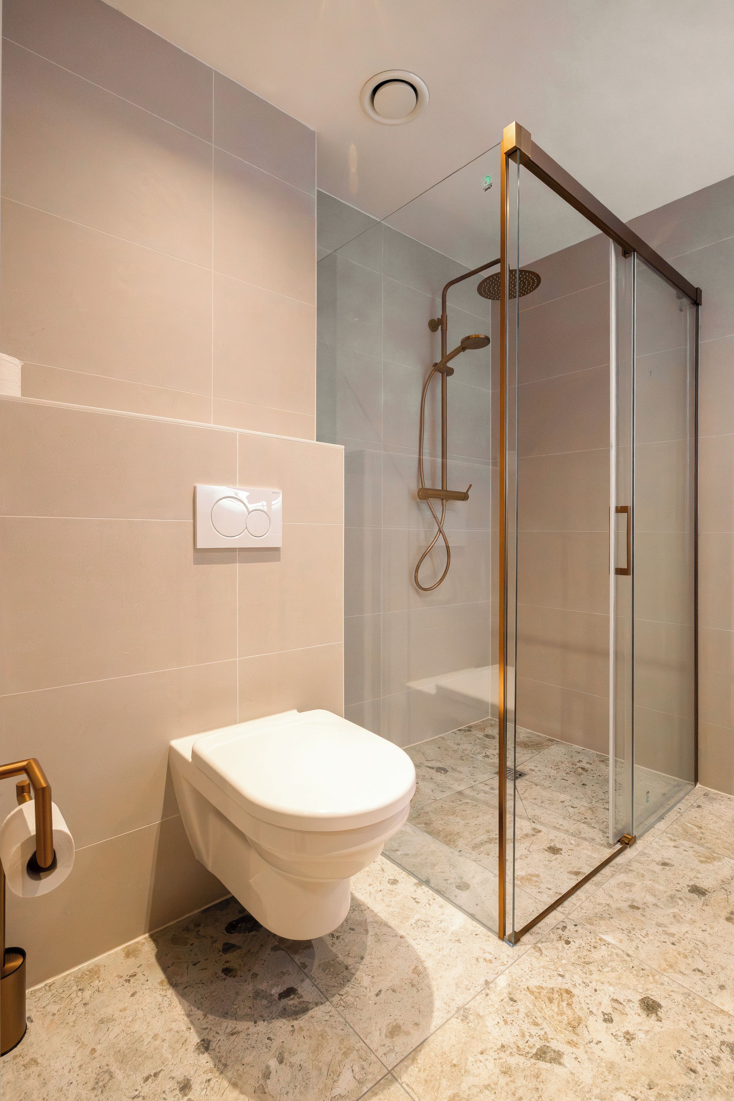 A modern bathroom with a toilet, a glass shower enclosure, and a marble floor.