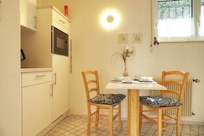 A small kitchen with a microwave, a table with chairs, and a window with curtains. - Apartment 56m2 for two - wellness with DreiWeltenCard - quiet & central (Bad Dürrheim)