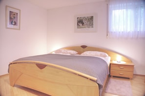 A bedroom with a wooden bed, a bedside table, a nightstand, a rug, and two framed pictures on the wall. - Apartment 56m2 for two - wellness with DreiWeltenCard - quiet & central (Bad Dürrheim)