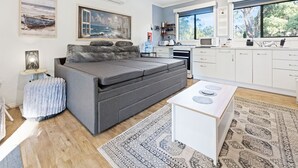 Un saló modern amb un sofà, una taula petita, una zona de cuina amb armaris blancs i obres d'art a les parets.