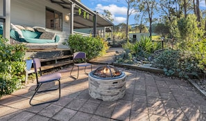 Eine Terrasse mit Feuerstelle, Gartenmöbeln und einem überdachten Bereich mit einer Couch.