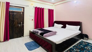 A bedroom with a bed, curtains, a ceiling fan, and a patterned rug. - Vandana Palace (Ayodhya)