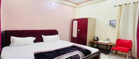 A hotel room with a bed, a desk, a chair, a wardrobe, and a ceiling fan.