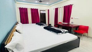 A hotel room with a bed, a desk, a chair, and a ceiling fan. - Vandana Palace (Ayodhya)