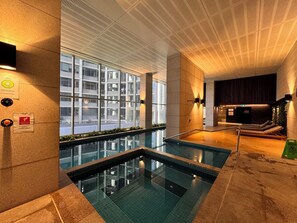 Ein moderner, überdachter Poolbereich mit großen Glaswänden und einer Rasterdecke, mit Blick auf ein Gebäude.