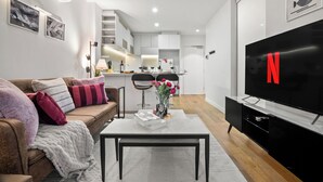 A modern living room with a sofa, coffee table, and a flat-screen TV. - Luxury Apartment | 2BR City Views | Gym+Pool+Spa+Sauna (Melbourne)