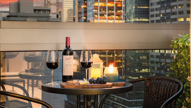 A balcony with a table set for two, featuring a bottle of wine, glasses, a candle, and grapes. - Luxury Apartment | 2BR City Views | Gym+Pool+Spa+Sauna (Melbourne)