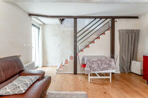 A room with a brown leather sofa, a small table with a patterned tablecloth, a staircase with a metal railing, and a red cabinet. - Cottage 'Gîte Chez Augustine' with Wi-Fi and Air Conditioning (Sarrians)