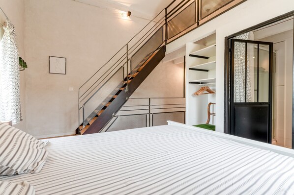A bedroom with a bed, a staircase, a wardrobe, and a door leading to another room. - Cottage 'Gîte Chez Augustine' with Wi-Fi and Air Conditioning (Sarrians)