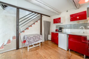 A compact kitchen with a dining area, a staircase, and a red appliance. - Cottage 'Gîte Chez Augustine' with Wi-Fi and Air Conditioning (Sarrians)