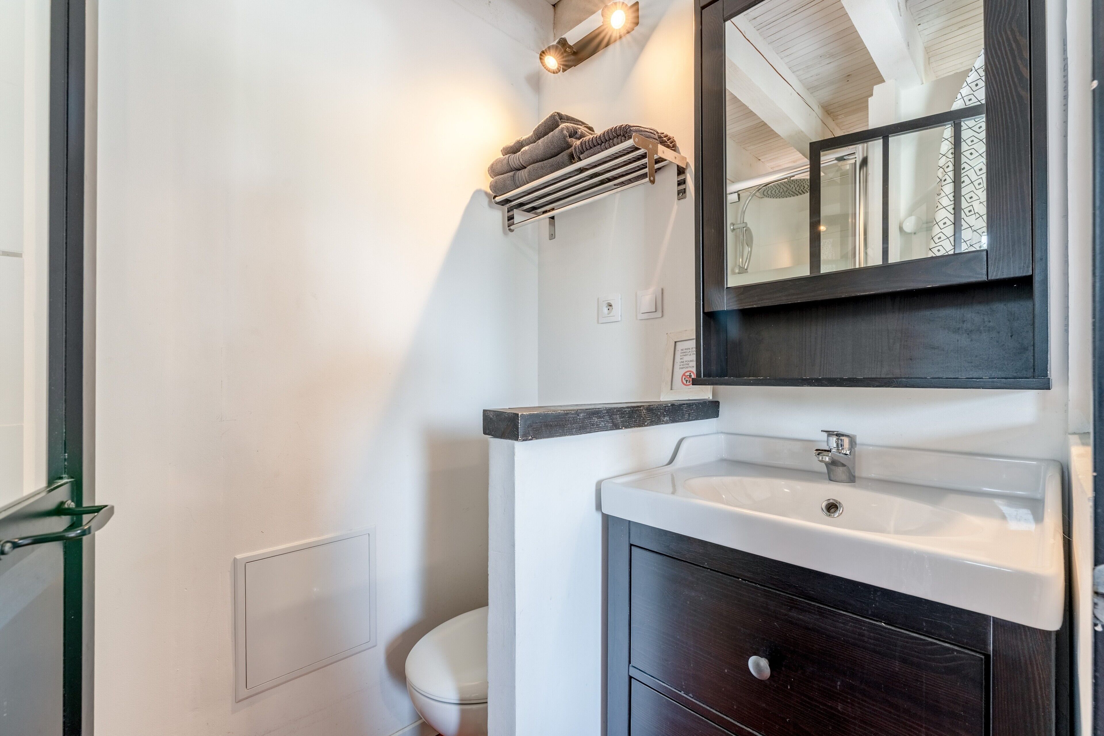 Une salle de bain avec un lavabo blanc, un meuble-lavabo en bois foncé, un porte-serviettes et un miroir.