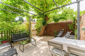 A covered outdoor patio with a table and chairs, surrounded by greenery and a bamboo fence. - Cottage 'Gîte Chez Augustine' with Wi-Fi and Air Conditioning (Sarrians)