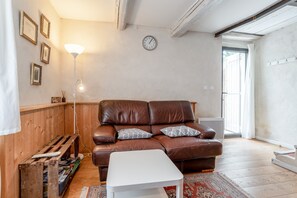 Un salon avec un canapé en cuir marron, une table basse blanche, un banc en bois et une horloge au mur.