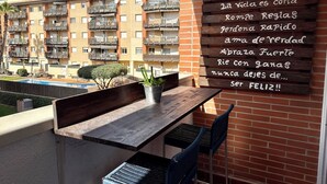 A balcony with a wooden table and chairs, a potted plant, and a sign with a message. - Fenals Family Apartment with Pool (Lloret de Mar)