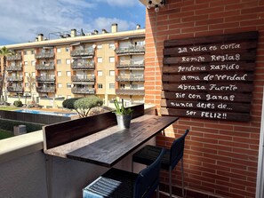 Ein Balkon mit Holztisch und Stühlen, einer Topfpflanze und einem Schild mit einer Aufschrift.