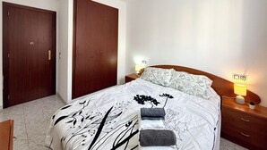 A bedroom with a bed, two wooden wardrobes, a bedside table with a lamp, and a nightstand with a lamp. - Fenals Family Apartment with Pool (Lloret de Mar)