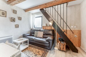 A living room with a brown leather sofa, a white table, a patterned rug, and a wooden staircase. - Cottage 'Gîte Chez Augustine' with Wi-Fi and Air Conditioning (Sarrians)