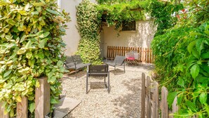 Un patio con mobiliario exterior, cercado por una valla de madera y una pared cubierta de plantas trepadoras.