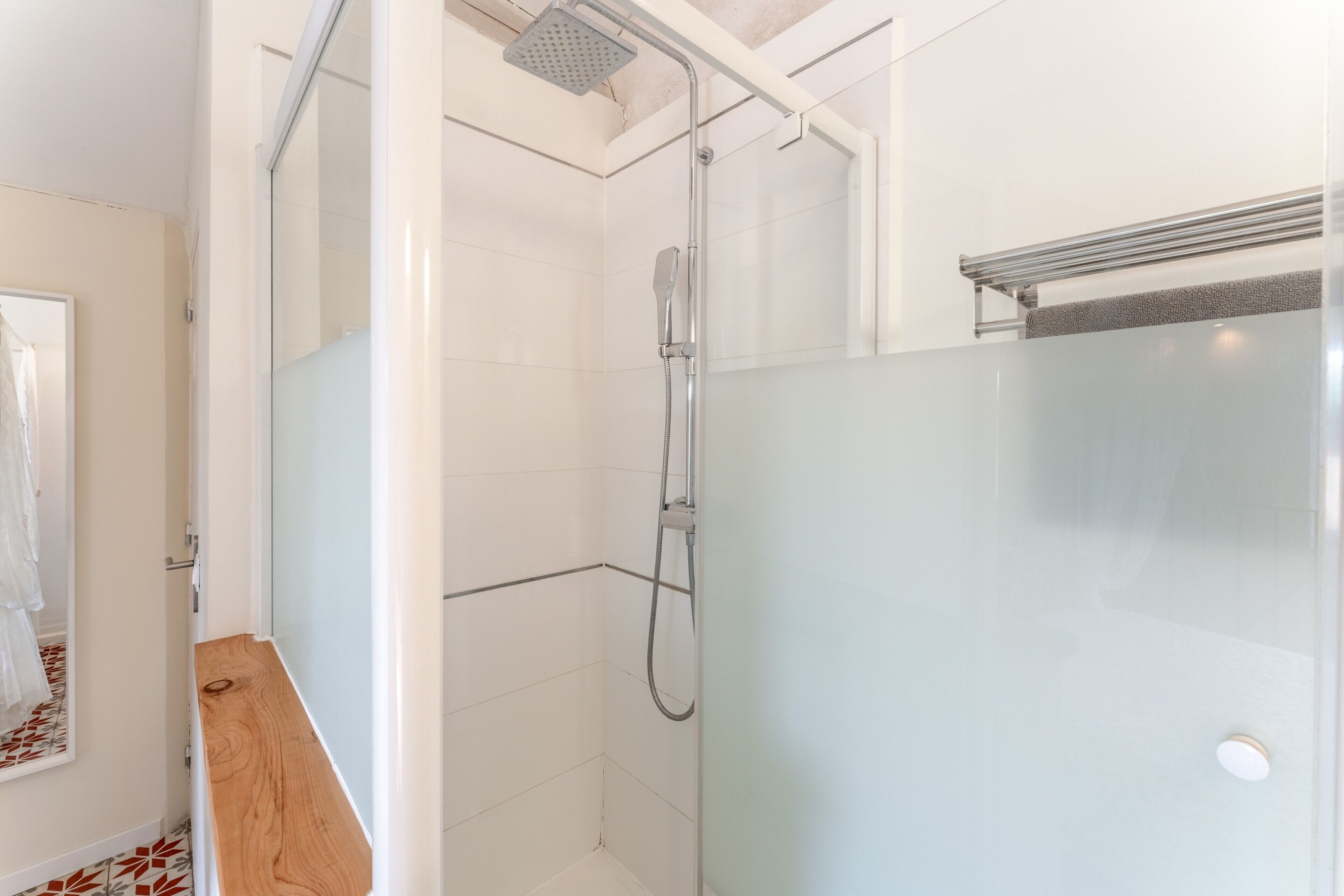 Un bagno moderno con box doccia in vetro, mobile lavabo in legno e pavimento rivestito di piastrelle bianche.