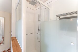 Een moderne badkamer met een douchecabine van glas, een houten wastafelmeubel en een vloer met witte tegels.