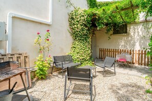 Een terras buiten met metalen stoelen, een barbecue en een muur begroeid met klimplanten.