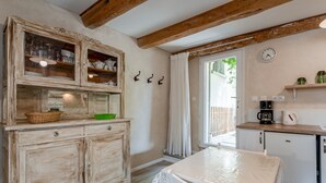 Una cocina rústica con armarios de madera, una mesa con cubierta de plástico, una cafetera y un reloj en la pared.