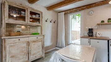 Eine rustikale Küche mit Holzausbau, einem Tisch mit Plastikdecke, einer Kaffeemaschine und einer Uhr an der Wand.