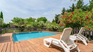 Una terraza de madera con piscina, sillas de descanso blancas y valla de madera.