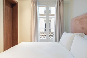 A hotel room with a bed, curtains, a wooden wardrobe, and a view of a balcony. - The Boissy 1 (Paris)