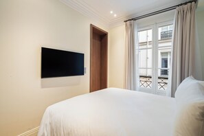 A hotel room with a bed, a mounted TV, a door, and a balcony view. - The Boissy 1 (Paris)