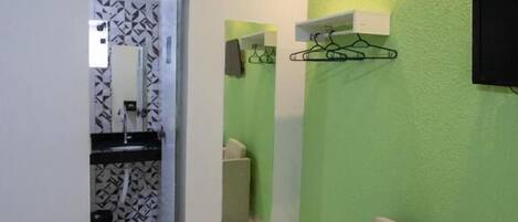 A room with a green wall, a beige chair, a mirror, a coat rack, and a television.