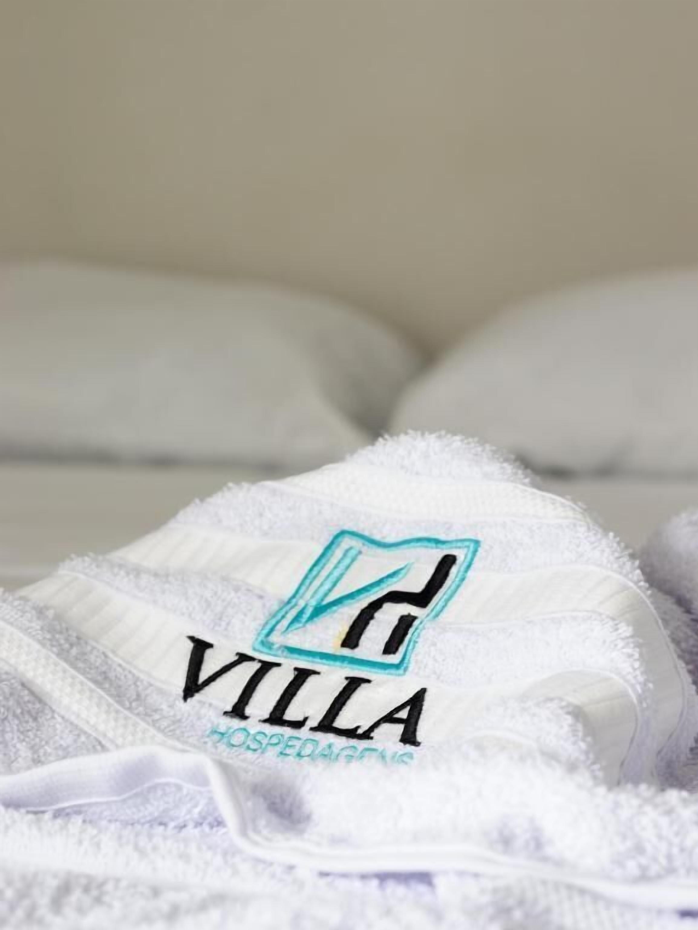 Una toalla blanca con un logo y el texto 'VILLA' y 'OSPEDAGENS' sobre una cama.