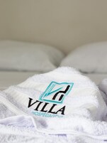 Toalha branca com um logotipo e o texto 'VILLA' e 'OSPEDAGENS' sobre uma cama.