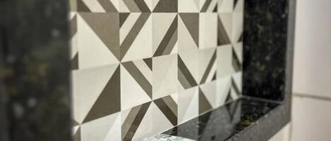 Casa de banho com bancada preta e painel de azulejos geométricos.