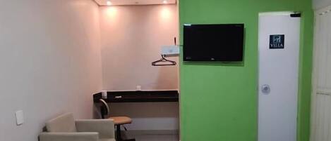 Habitación de hotel con dos camas, un escritorio, una silla, un televisor y una pared de acento verde.