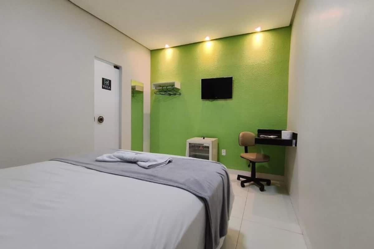 Una habitación de hotel con una cama, un escritorio, una silla, un televisor y una pared verde.