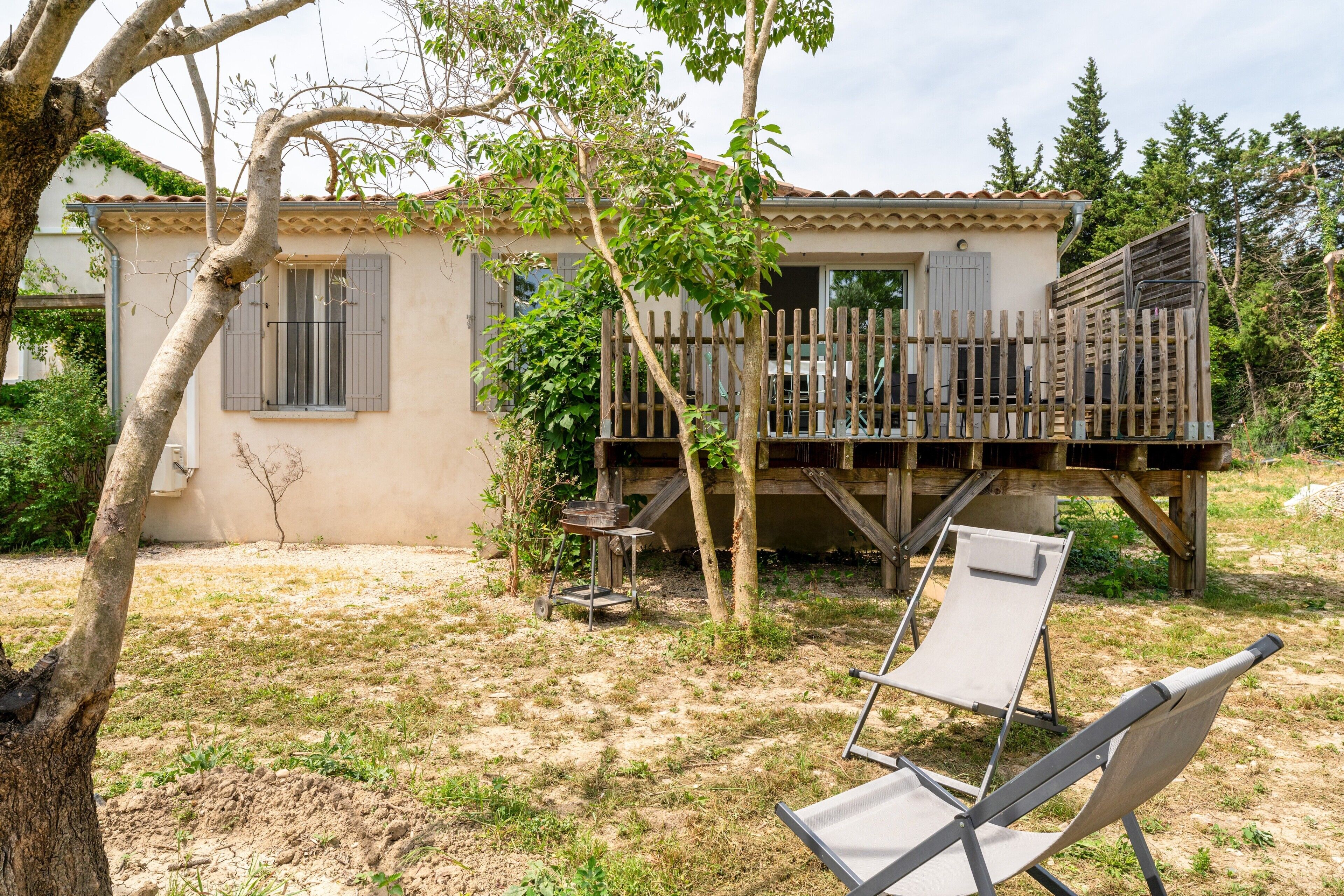 A house with a wooden deck, a small outdoor grill, and a chair.