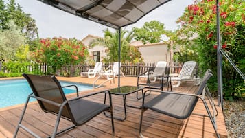 A poolside area with lounge chairs, a table, and a pergola.