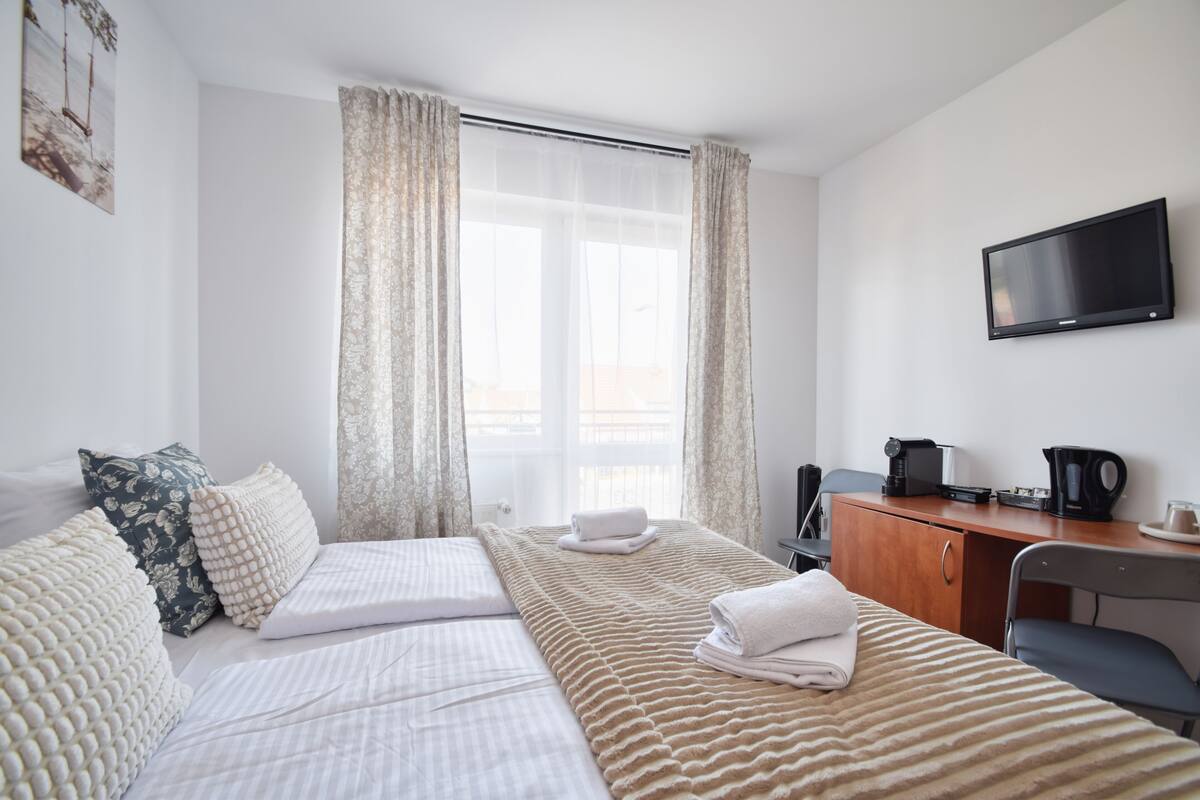 Hotellihuone, jossa on sänky, työpöytä, televisio ja ikkuna, jossa on verhot.
