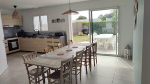Een moderne keuken met houten kastjes, een eettafel met stoelen en uitzicht op de achtertuin door glazen deuren.