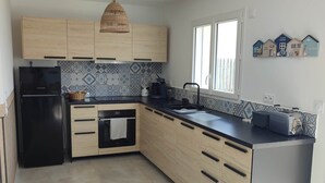 Een moderne keuken met houten kastjes, een zwarte koelkast, een eettafel met stoelen en een groot raam.