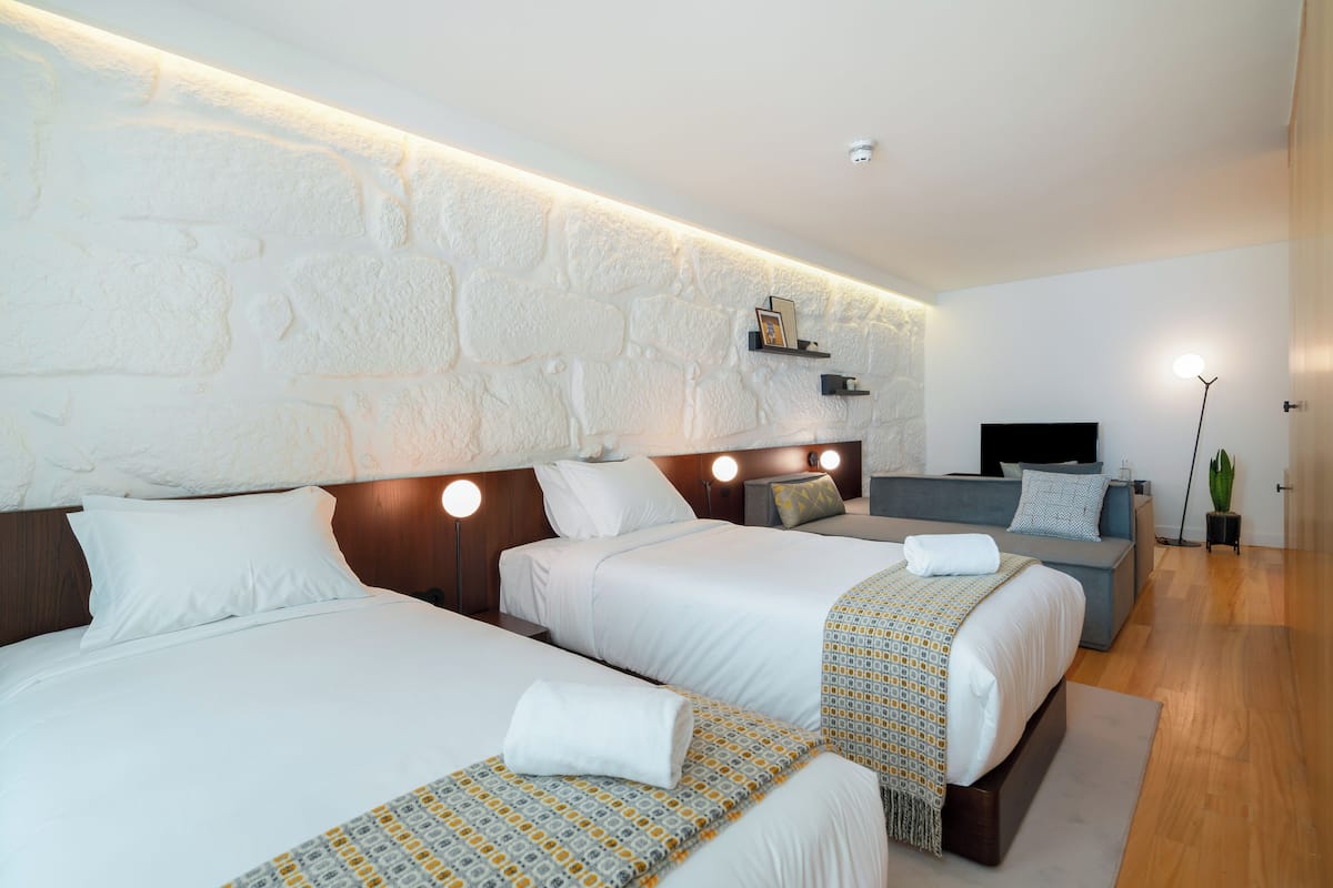 A hotel room with two beds, a sofa, a TV, and a stone wall.