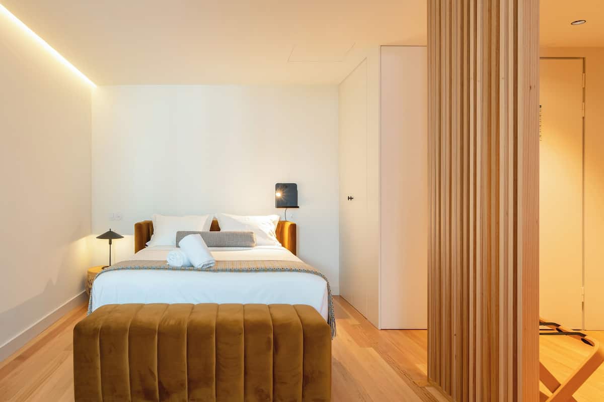 A modern bedroom with a large bed, a wooden floor, a wall-mounted light, and a wooden partition.