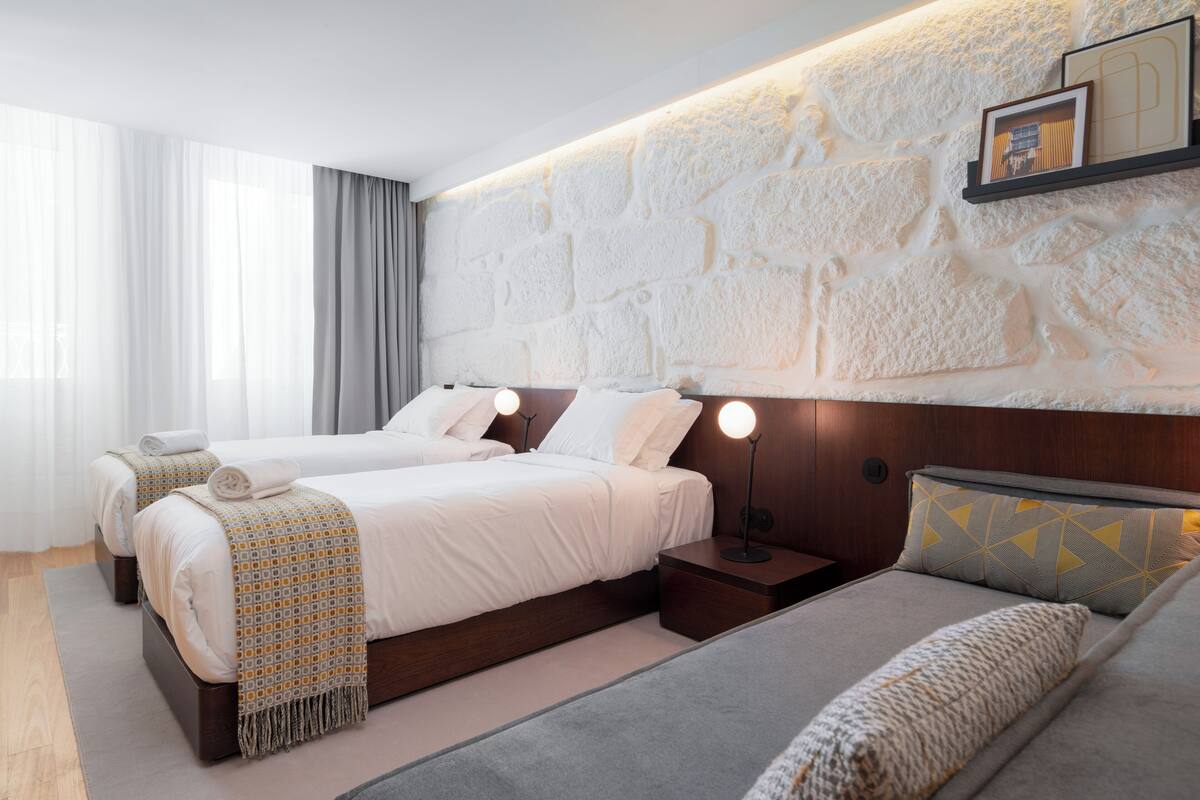 A modern hotel room with two beds, a stone accent wall, and a cozy seating area.
