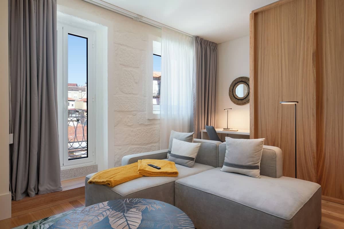 A modern hotel room with a sofa, a small table, and a view of the city through the window.