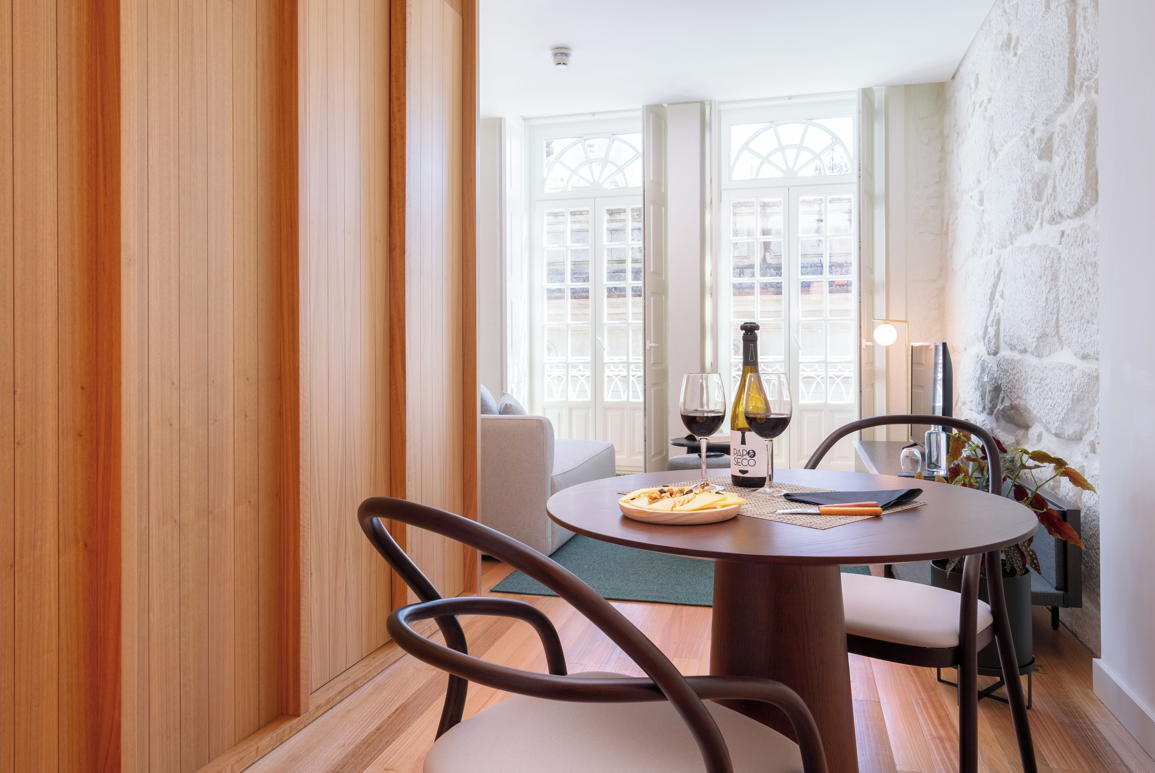 A dining area with a round table, chairs, a bottle of wine, and a plate of food.