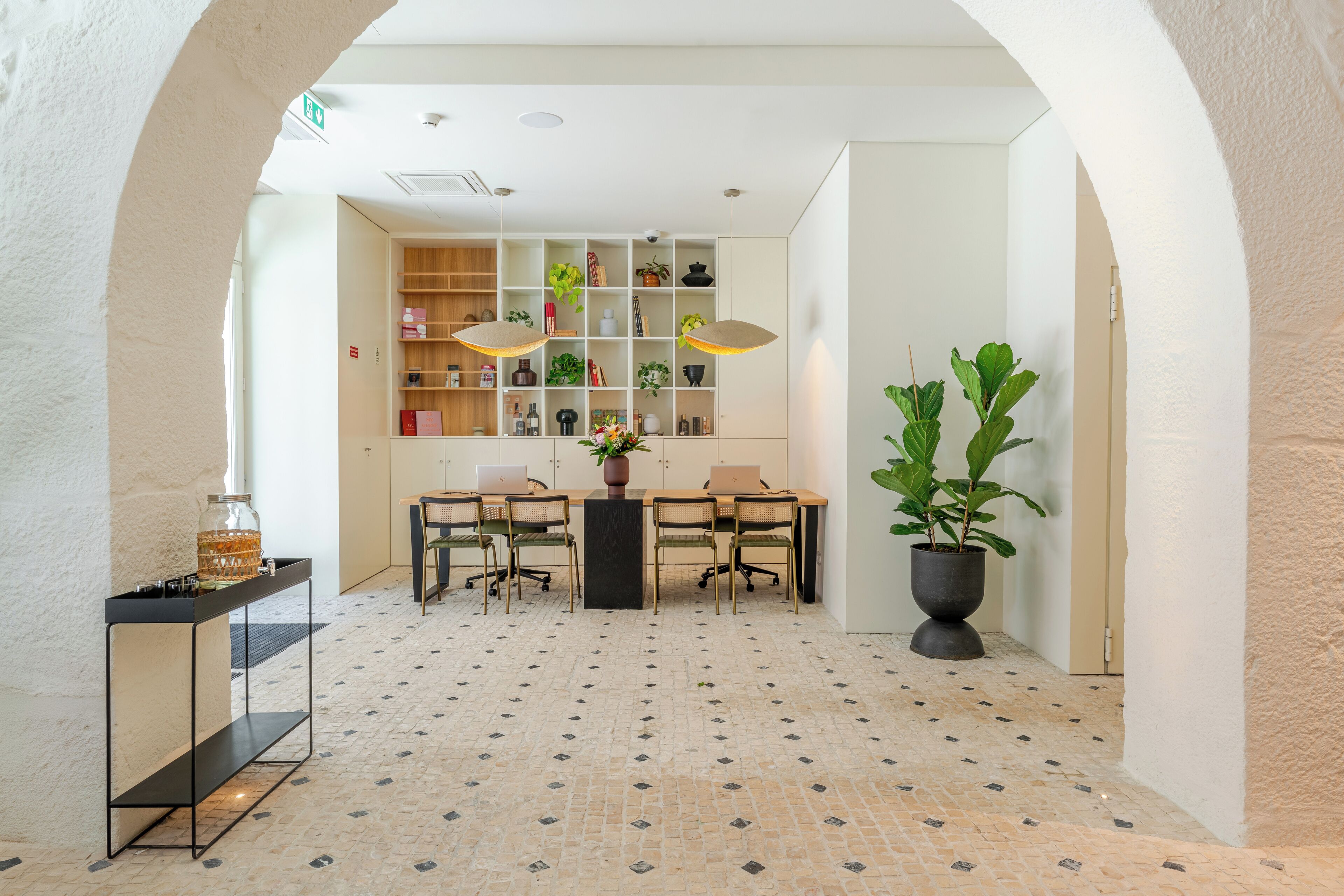 A modern interior with a central table, chairs, a potted plant, and shelves with various items.