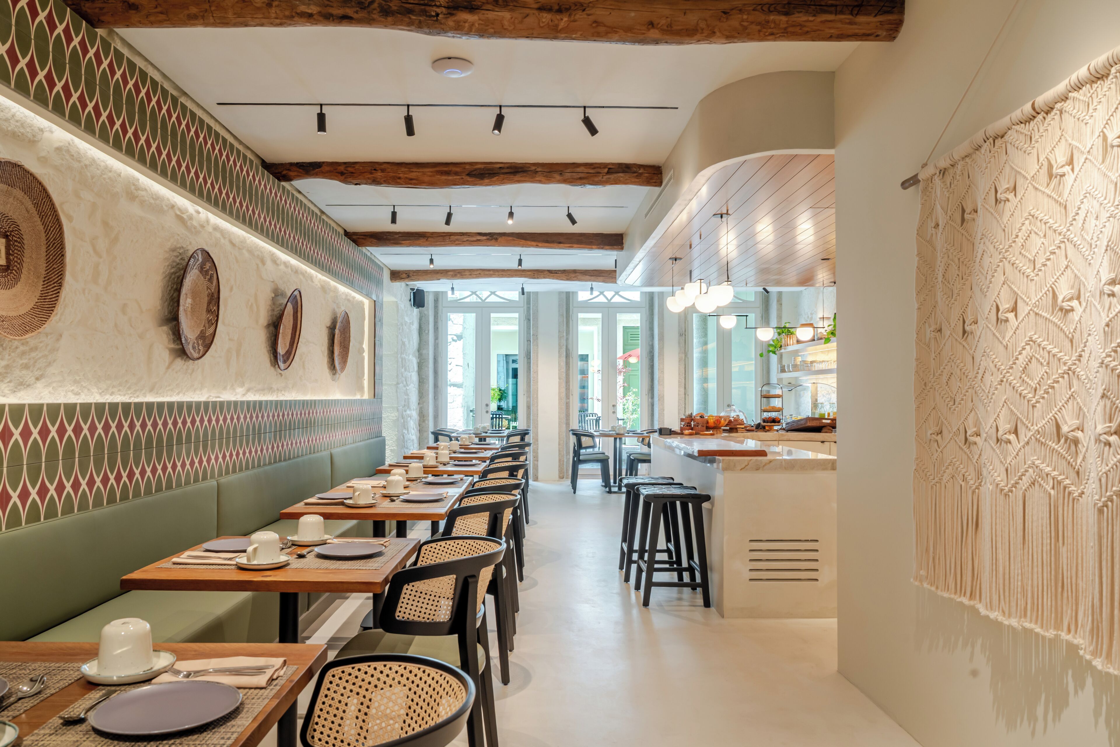 A restaurant with long wooden tables, green cushioned booths, and a patterned wall.